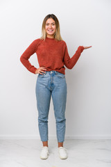 Full body young caucasian woman showing a copy space on a palm and holding another hand on waist.