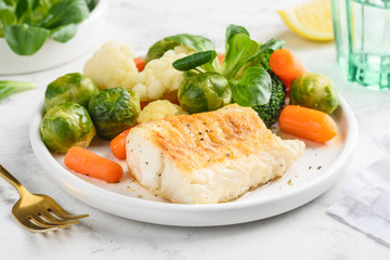 Fried cod fillet with vegetables: baby carrots, brussels sprouts, broccoli, cauliflower and corn...