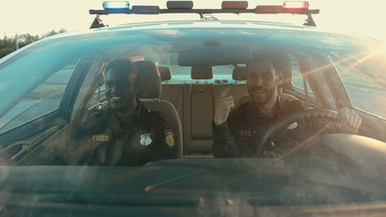 Two sociable policemen best friends talking together while driving a patrol car to the road accident at daytime. Patrol in the city. © Fractal Pictures