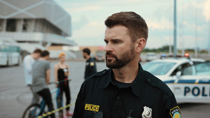 Attractive serious police officer finding illegal drugs talking walkie-talkie with colleagues staying at crime scene area outdoors. People in background walking and looking around.