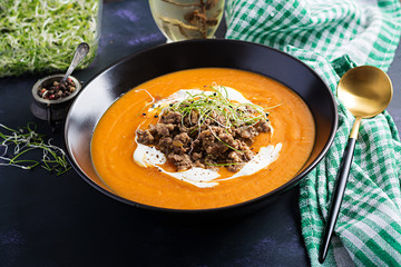 Delicious cream of pumpkin soup with roasted forcemeat made of beef minced meat in a bowl on a dark table. Thanksgiving Day.