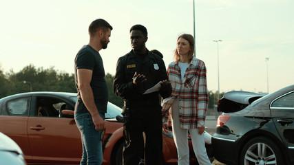 Baffled young people man and woman upset with car accident. Two drivers talking about the situation to policemen. Investigation process. Police on duty.