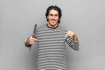 Fototapeta premium Young employee man holding an inventory points down with fingers, positive feeling.