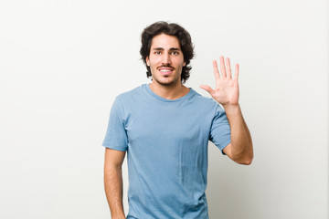 Fototapeta premium Young handsome man against a white background smiling cheerful showing number five with fingers.