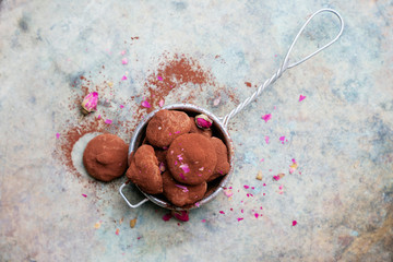 Chocolate candy truffles in tea strainer sprinkled with cocoa dust and flower petals over rustic...