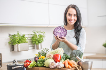 Cheerful young woman with red cabbage and fresh vegetables in her kitchen preparing a healthy lunch