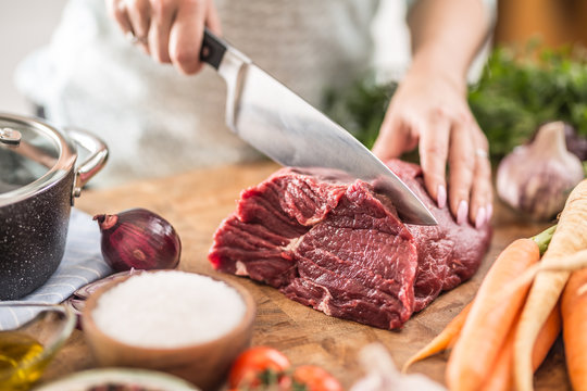 Young housewife slicing fresh beef steak. Female hands preparing lunch of meat and vegetables