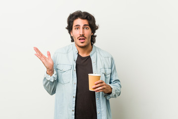 Young cool man drinking a coffee surprised and shocked.