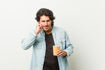 Young cool man drinking a coffee covering ears with hands.