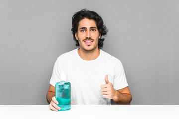 Young man holding a mouthwash smiling and raising thumb up