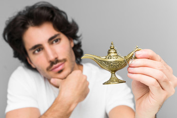 Young caucasian man holding a magic lamp isolated on a grey background