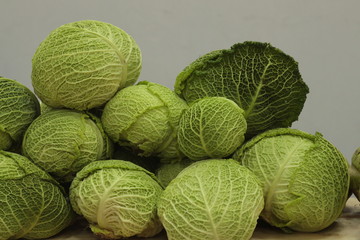 A large pile of green heads of cabbage lies on a store counter.