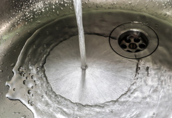 Running water out of a water tap in a metallic kitchen sink 