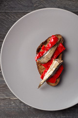 Fish sandwiches with sprats. Sandwich with red bell pepper and sprats on a gray plate. A set of sandwiches with sprats Close-up photo. Seafood. View from above. Top view.