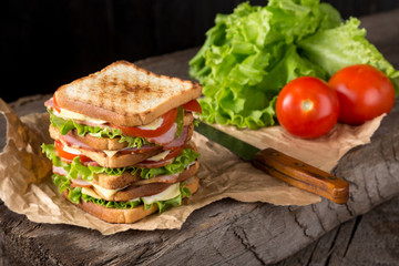 Delicious sandwich with ham, cheese, tomatoes, lettuce. High club sandwich with toast. close up of fresh sandwich with ham, bacon,tomatoes,cheese and lettuce On a wooden board. Sandwich bread tomato, 