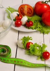 mozzarella cheese, red tomatoes and lettuce on a plate on a light wooden table. Weight loss, diet, proper nutrition, healthy lifestyle