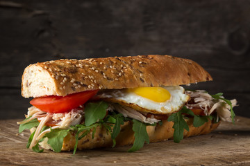 Delicious sandwiches on a dark wooden table. Sandwiches with tomatoes, chicken breast, arugula and egg. Yolks flowing. Homemade sandwich with fresh tomatoes and chicken breast. close-up photo