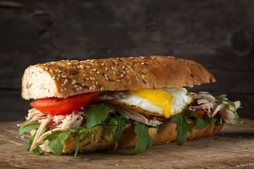 Delicious sandwiches on a dark wooden table. Sandwiches with tomatoes, chicken breast, arugula and egg. Yolks flowing. Homemade sandwich with fresh tomatoes and chicken breast. close-up photo