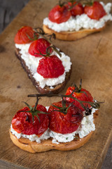 Sandwiches on a dark wooden table. Sandwiches with feta and baked cherry tomatoes. Delicious bruschetta with tomatoes, feta cheese, dill and spice on wooden board close-up photo. Feta, tomato and bals