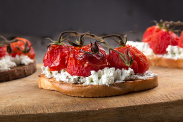 Sandwiches on a dark wooden table. Sandwiches with feta and baked cherry tomatoes. Delicious bruschetta with tomatoes, feta cheese, dill and spice on wooden board close-up photo. Feta, tomato and bals