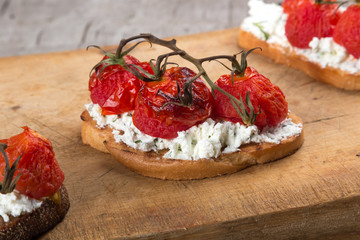Sandwiches on a dark wooden table. Sandwiches with feta and baked cherry tomatoes. Delicious bruschetta with tomatoes, feta cheese, dill and spice on wooden board close-up photo. Feta, tomato and bals