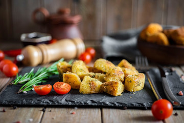 Spicy potatoes baked in the oven on a gray dish with herbs and tomatoes on a wooden table