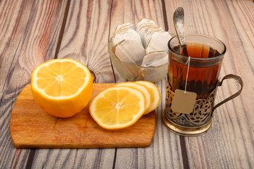 Tea in a faceted glass in a vintage Cup holder, tea bags in a glass vase and sliced lemon on a Board on a wooden background. Close up.