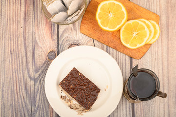 Tea in a faceted glass in a vintage Cup holder, tea bags in a glass vase, sliced lemon on a Board and a piece of waffle cake on a white plate on a wooden background. Close up.