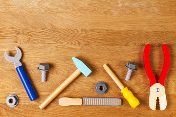 Wooden kids toys screwdriver, plier, bolts, nuts and other construction tools frame on wood background. Top view, flat lay