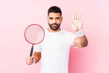 Young arabian man playing badminton isolated standing with outstretched hand showing stop sign, preventing you.