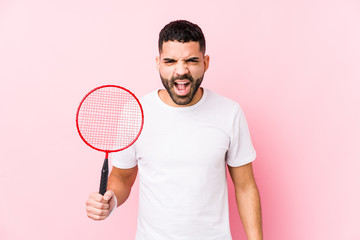 Young arabian man playing badminton isolated screaming very angry and aggressive.