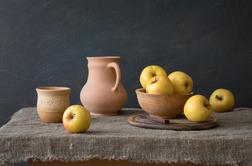 A set of pottery, yellow apples on the table. Still life in rustic style. Natural light from the window.