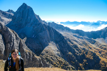 Naklejka premium Woman with big hiking backpack walking on a pathway to reach the Grosse Gamswiesenspitze in Lienz Dolomites, Austria. Sharp peaks in the back, and a valley covered with clouds. Massive Alpine mountain