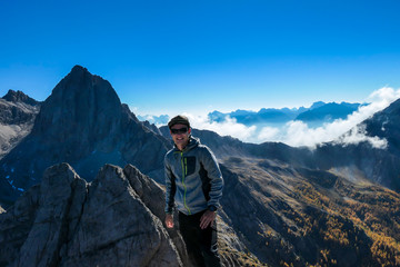 A man standing on the top of Grosse Gamswiesenspitze in Lienz Dolomites, Austria. Sharp, dangerous slopes. Massive Alpine mountains. Solo wanderer. He is happy and proud of his achievement. Freedom