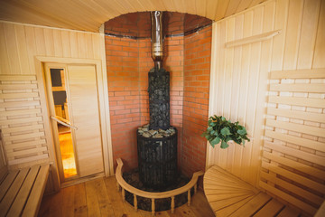 The big round stone furnace in a sauna. The walls trimmed with a red brick and a tree from natural breeds