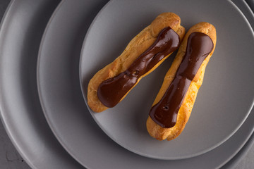 Tasty eclairs on a plate on a white wooden table. Served with flowers. Rectangular gray plate....
