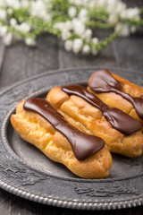 Tasty eclairs on a plate on a white wooden table. Served with flowers. Rectangular gray plate. Traditional french eclairs with chocolate. Home made cake eclairs. Traditional eclairs, profitroles class