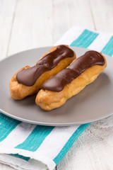 Tasty eclairs on a plate on a white wooden table. Served with flowers. Rectangular gray plate. Traditional french eclairs with chocolate. Home made cake eclairs. Traditional eclairs, profitroles class