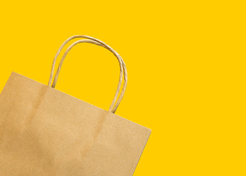 Blank brown paper shopping bag on yellow background. Spring Easter sale gift buying for holidays mothers womens day. Eco friendly natural recyclable materials zero waste concept