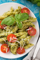 Pasta pesto with tomatoes on a blue table. Served with tomatoes, basil, olive oil, pesto, napkin, knife, fork. View from above. Top view. close-up photo