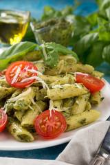 Pasta pesto with tomatoes on a blue table. Served with tomatoes, basil, olive oil, pesto, napkin, knife, fork. View from above. Top view. close-up photo