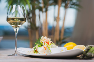 White fish seabass fillet with vegetables and white wine on a wooden table in a restaurant with decor.