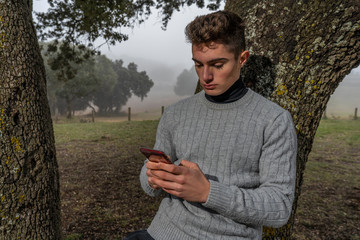 boy, young man chatting on a mobile phone, in a grey sweater in the countryside, thinking and enjoying nature