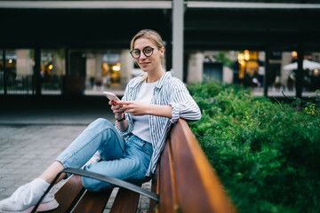 Smiling woman sitting on street bench with smartphone