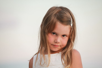 Serious blond little girl in white dress, close-up