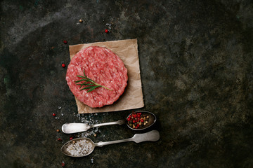 Raw Ground beef meat Burger steak cutlets with seasonings and herbs served over rustic metal background. Top view