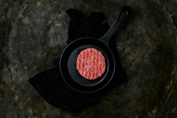 Raw Ground beef meat Burger steak cutlet with seasonings served on metal frying pan over the kitchen towel. Rustic metal background. Top view
