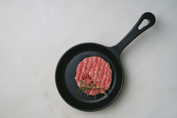 Raw Ground beef meat Burger steak cutlet with seasonings and rosemary served on metal frying pan over white marble background. Top view