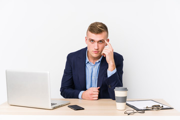 Young business man with a laptop pointing temple with finger, thinking, focused on a task.