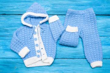Blue winter knitted baby clothes on blue wooden table background.